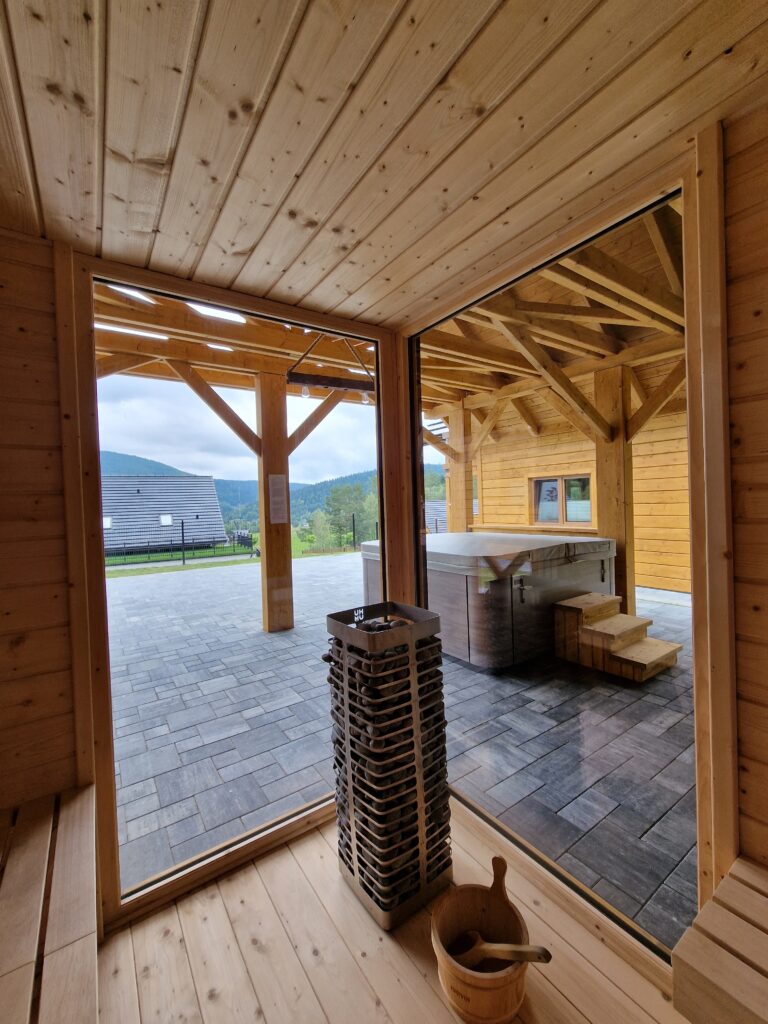 Widok z wnętrza nowoczesnej sauny w obiekcie Serce Beskidu na zewnętrzną strefę relaksu z jacuzzi, idealną na wyjazd integracyjny w góry, gdzie wspólny odpoczynek po szkoleniu sprzyja budowaniu relacji w zespole.
