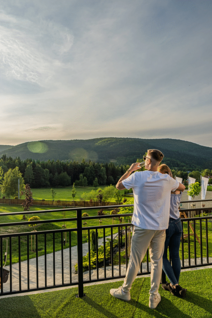 Widok na góry Beskidy z tarasu domu weselnego Serce Beskidu Para stoi na tarasie i obserwuje widok na góry Beskidy. W tle widać strefę wypoczynkową dla gości hotelu Serce Beskidu w otoczeniu zieleni.