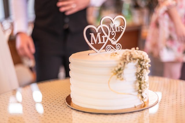 Mały, okrągły tort weselny z białym kremem i topperem z sercami "Mr & Mrs". To jest przykład tego, jak obniżyć koszt wesela na 100 osób w górach, wybierając mniejszy wypiek.