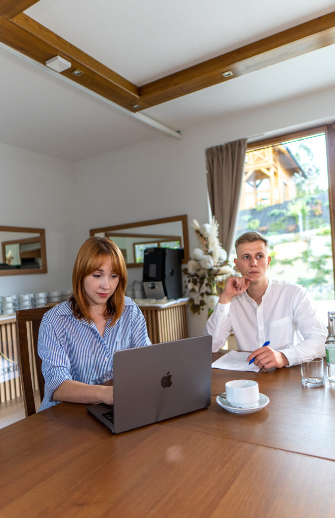 Dwie osoby siedzące przy drewnianym stole konferencyjnym w Serce Beskidu, pracujące na laptopach przy kawie, co ilustruje merytoryczne szkolenie jednodniowe w górach Beskidach w sali konferencyjnej hotelu Serce Beskidu.
