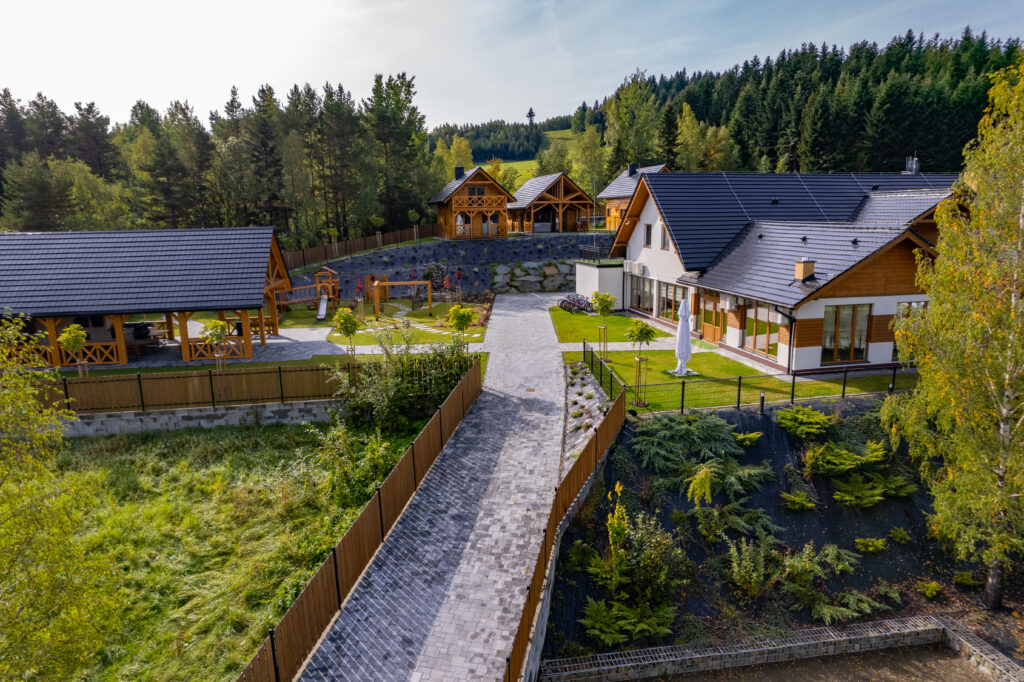 Widok na ośrodek Serce Beskidu, prezentujący nowoczesny budynek główny, drewniane domki całoroczne, altanę grillową oraz plac zabaw, co obrazuje idealne miejsce na warsztaty z noclegiem w górach Beskidu Wyspowego niedaleko Krakowa.