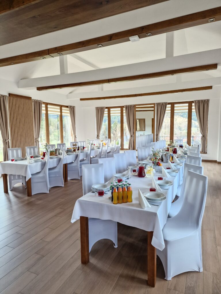 Widok na jasną, przestronną salę bankietową w restauracji Serce Beskidu, wyposażoną w długie, elegancko nakryte stoły z białymi obrusami, co stanowi idealne rozwiązanie, gdy zastanawiasz się, jak zorganizować chrzciny w restauracji dla większej liczby gości.