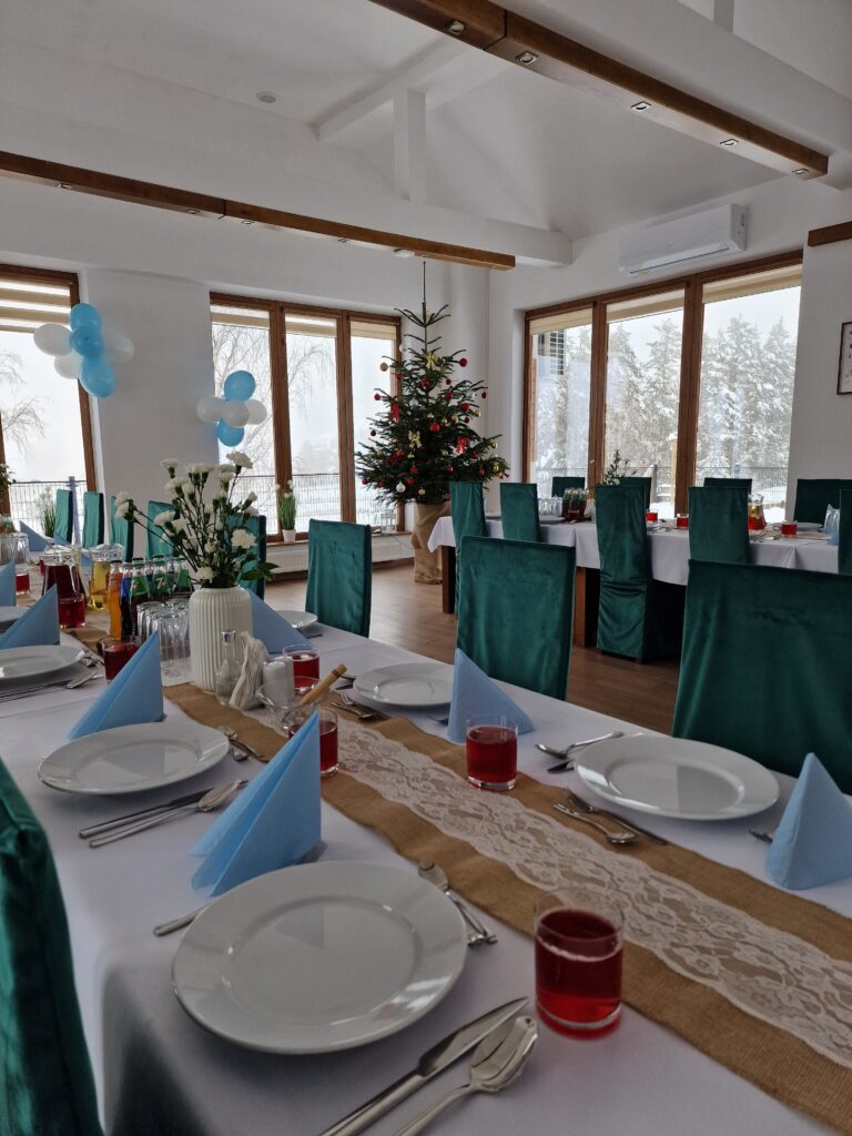 Przytulna sala restauracji Serce Beskidu z bożonarodzeniową choinką i zimowym widokiem za oknem, ukazująca możliwości organizacji klimatycznego przyjęcia chrzcielnego o każdej porze roku.
